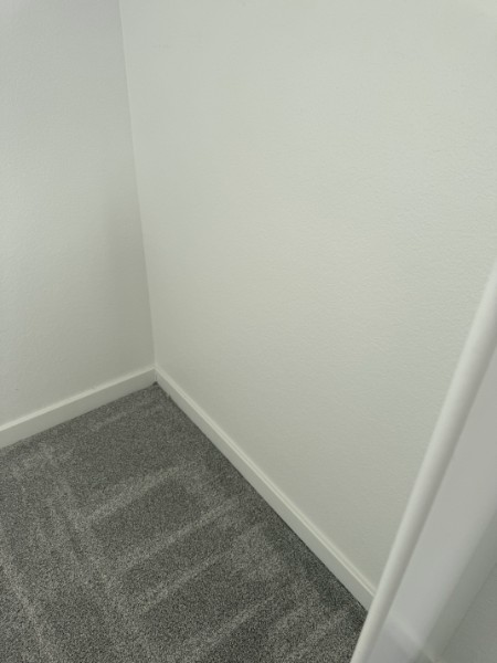Empty carpeted corner of a white room with baseboards and a doorway edge