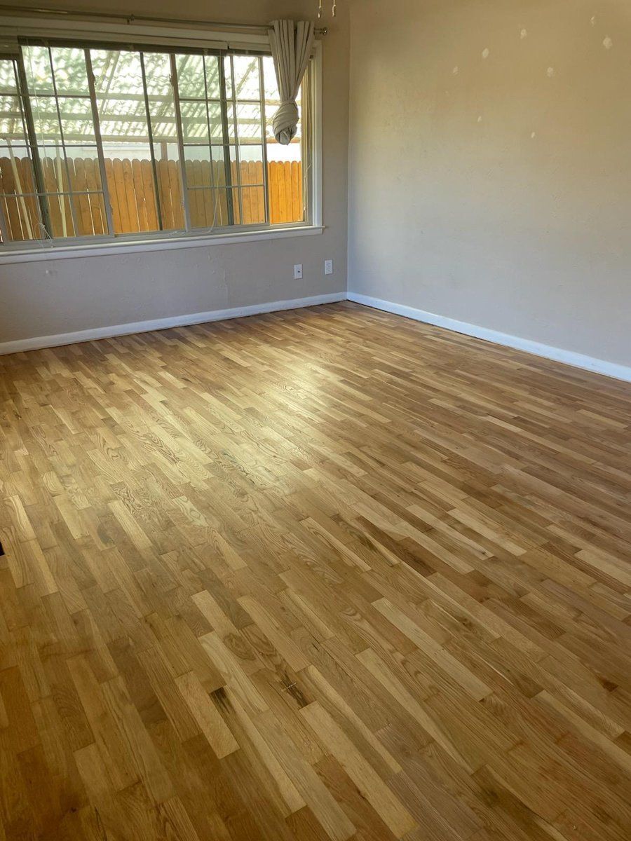 Empty room with hardwood floors, gray walls, and a large window.