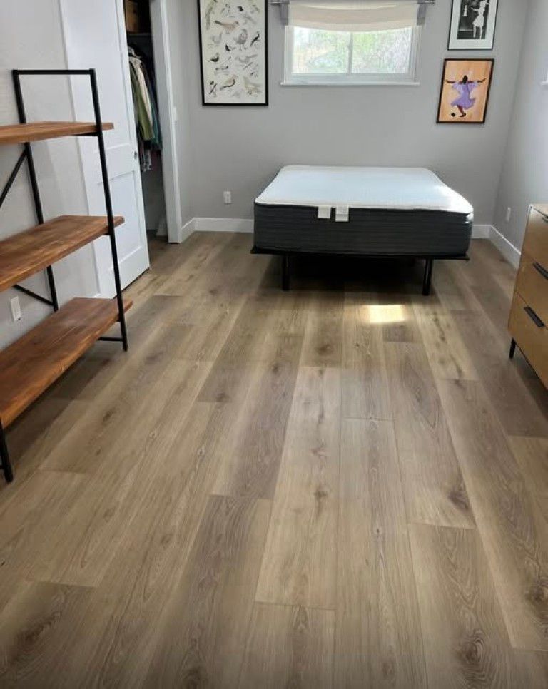 Minimal bedroom with bed, wood floor, shelves, dresser, and framed wall art.