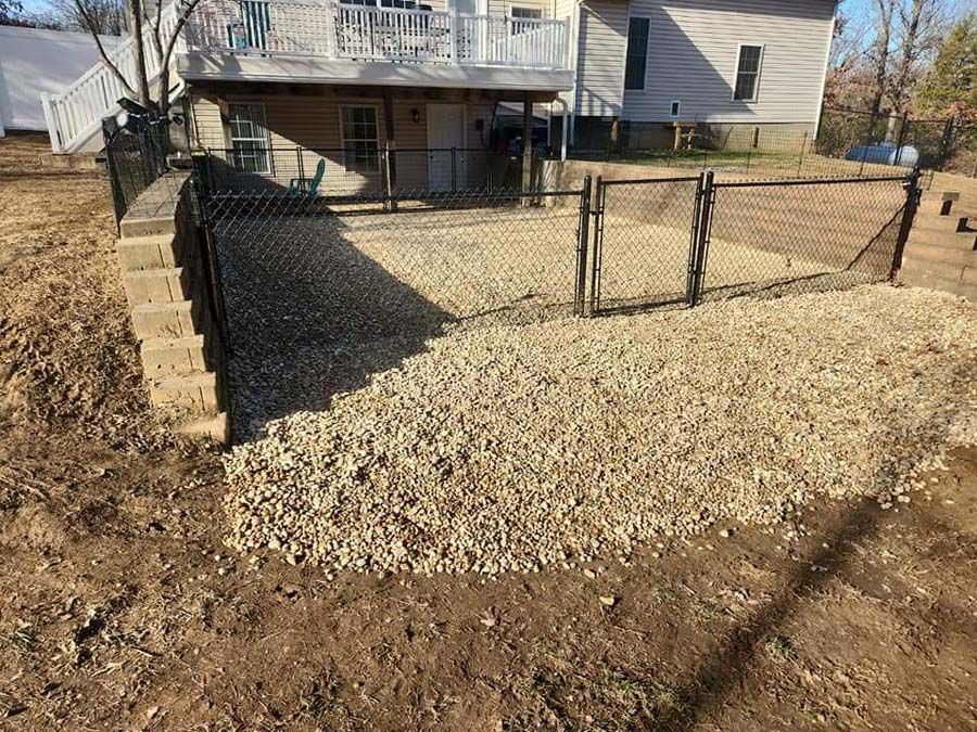 A chain link fence is surrounding a gravel area in front of a house.