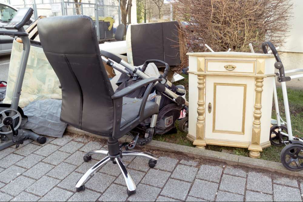 A black office chair is sitting on a brick sidewalk next to a dresser and a treadmill.