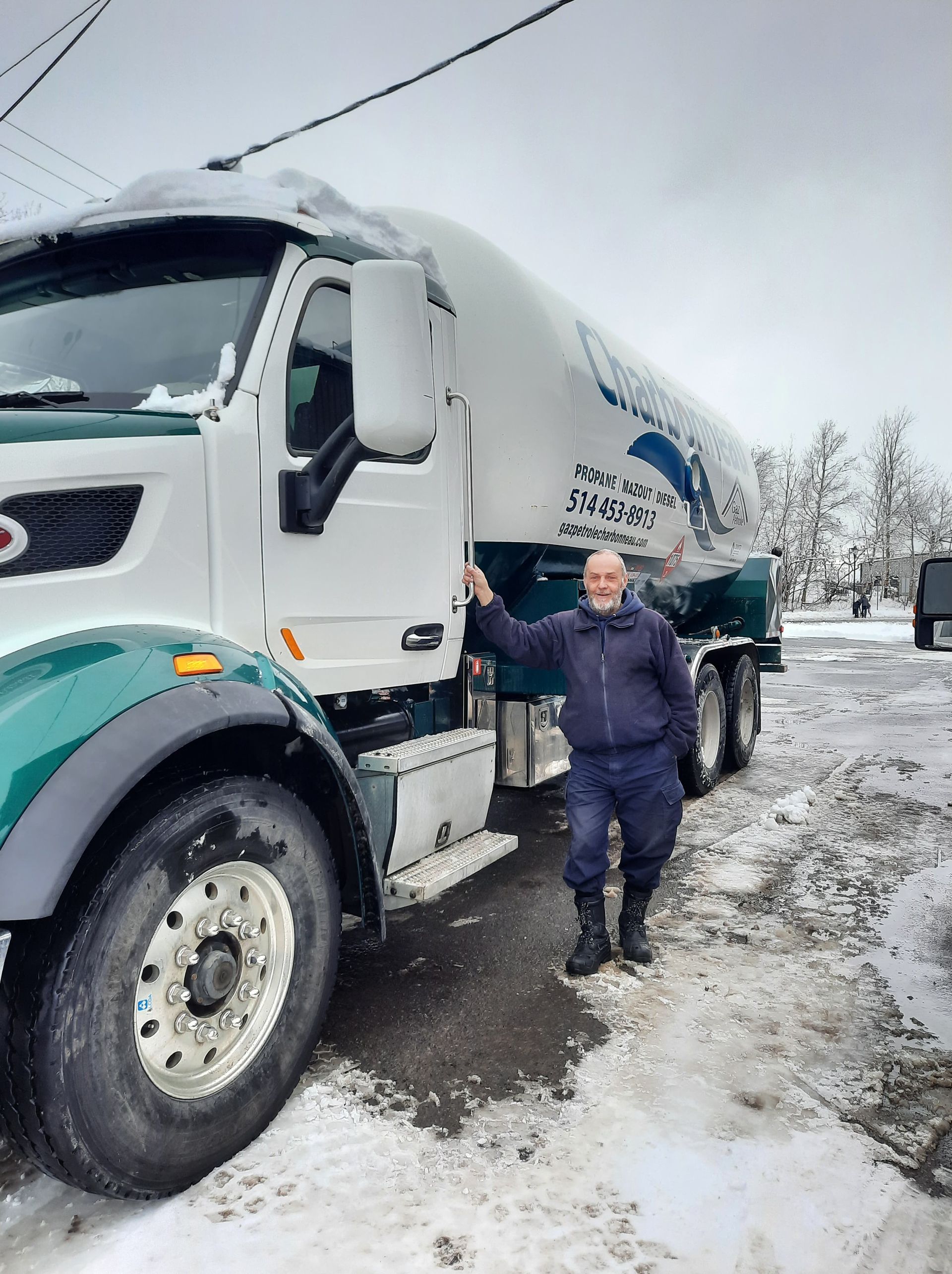Un homme se tient à côté d'un gros camion dans la neige.