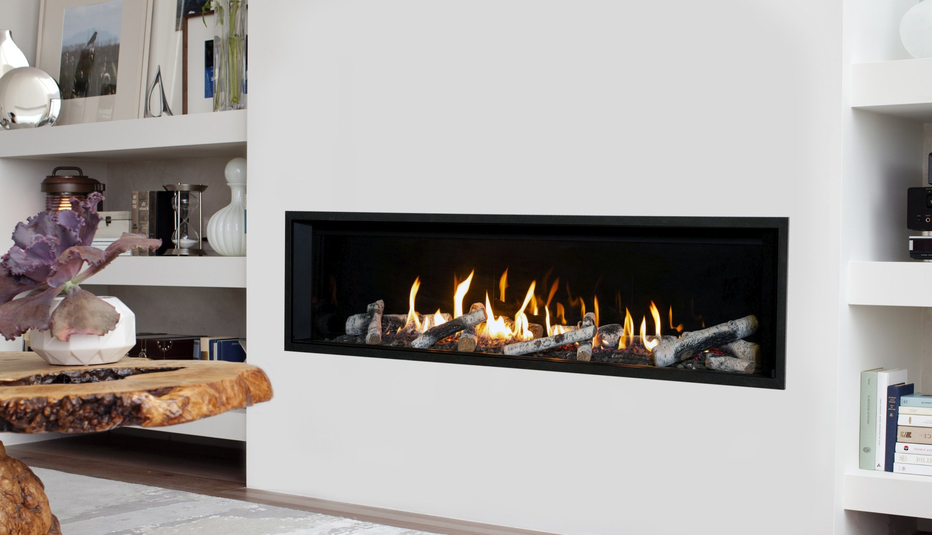 Cheminée moderne avec des flammes vacillantes et des bûches, encastrée dans un mur blanc.