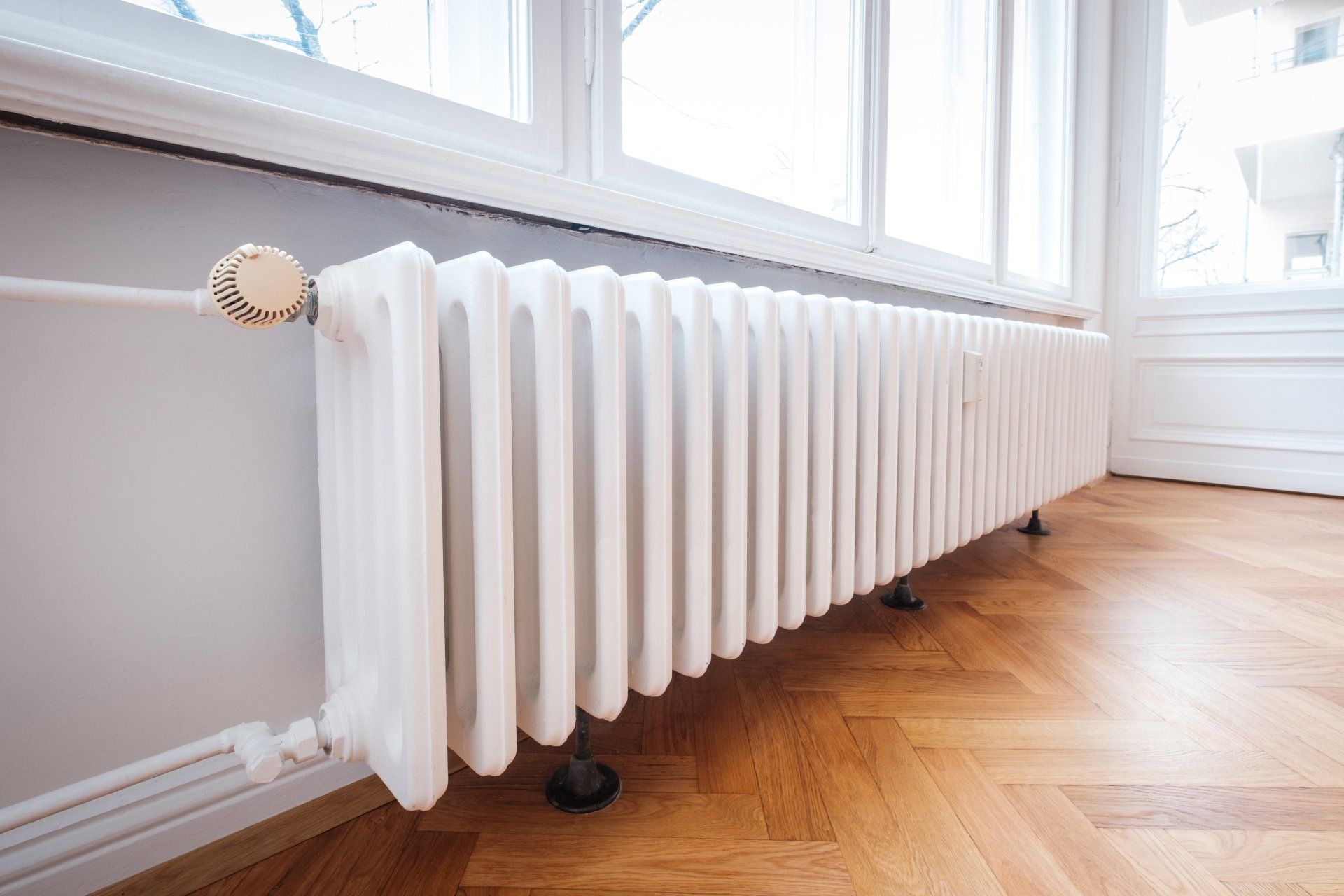 Radiateur blanc sous une fenêtre dans une pièce avec parquet.