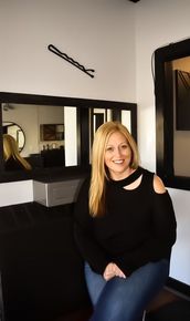 A woman is sitting on a stool in front of a mirror in a room.