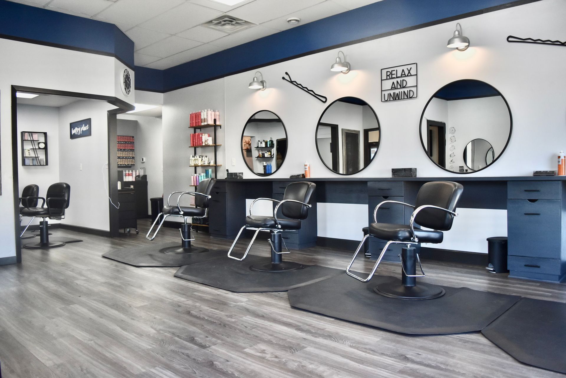 Hair salon interior with three styling stations, round mirrors, and black and blue accents.
