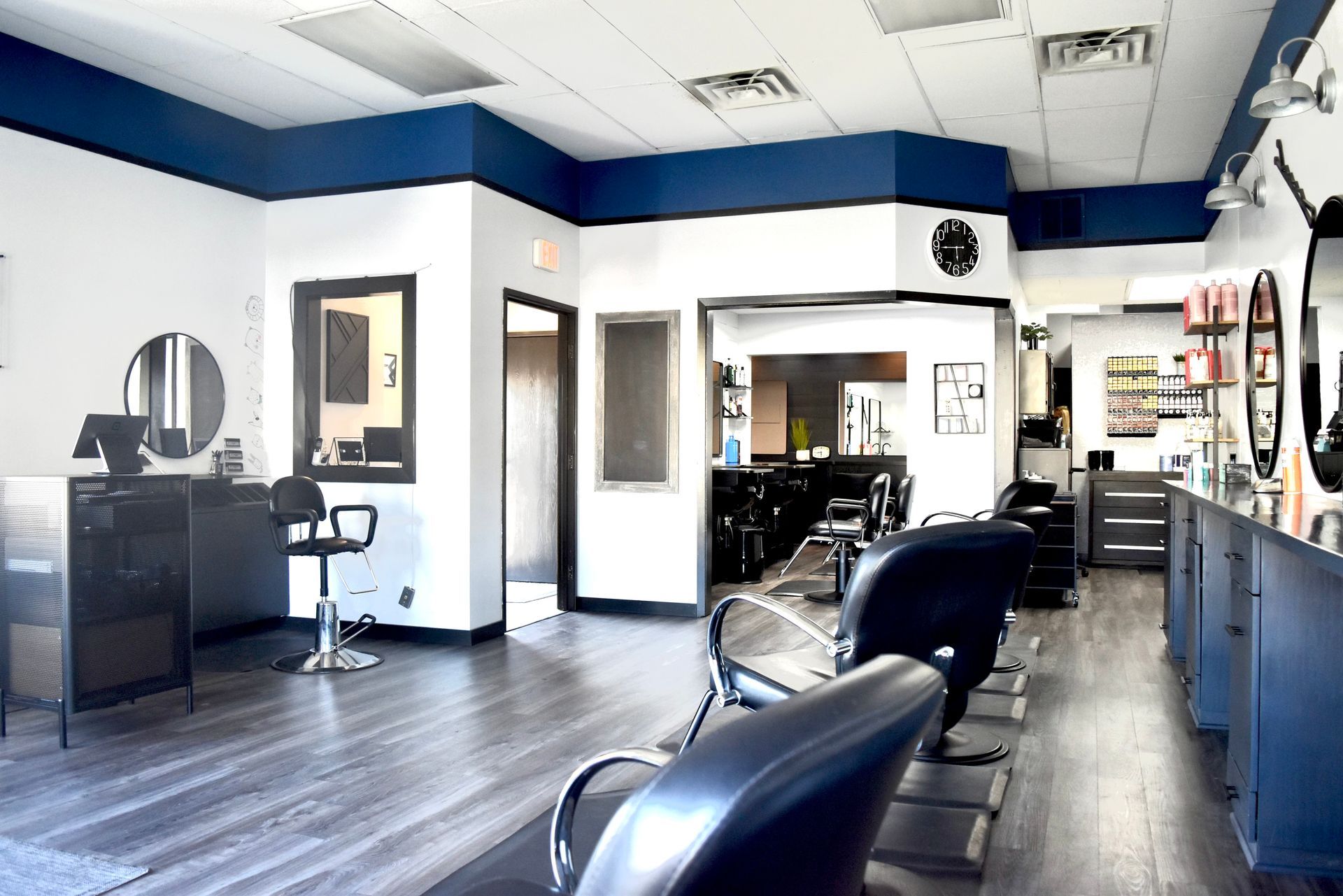 Hair salon interior, blue and white with dark wood floors, chairs, and styling stations.