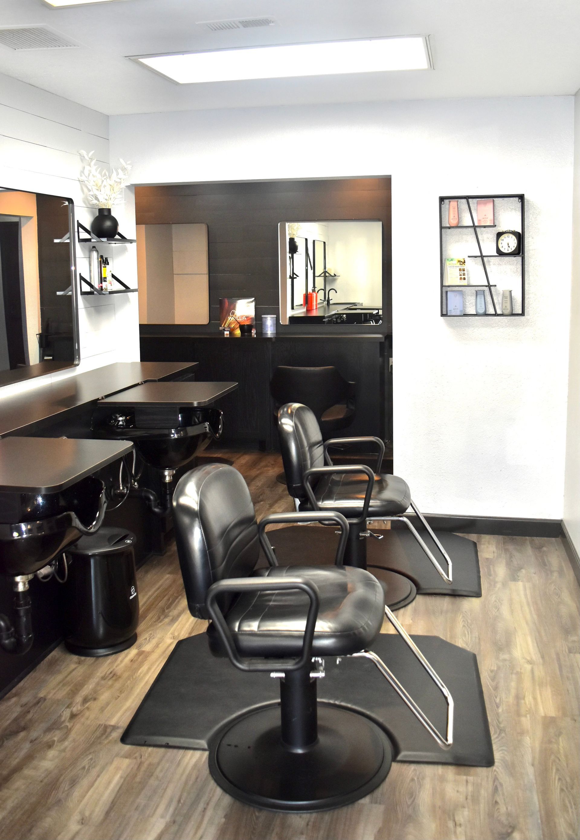 Salon interior with black chairs, stations, and accents, wooden floor, and bright overhead light.
