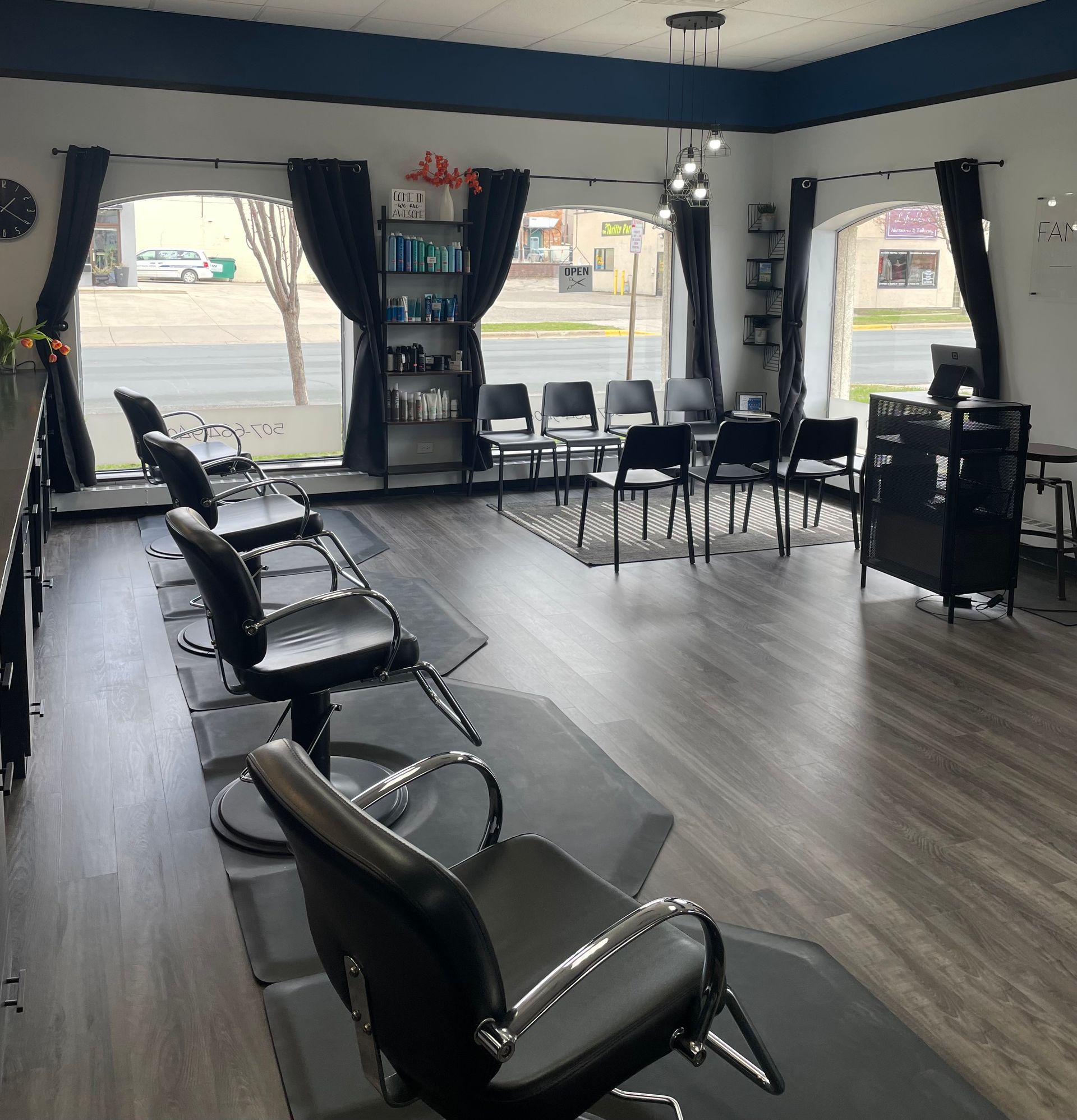 Hair salon interior with styling chairs, waiting chairs, and retail shelves, near street-view windows.
