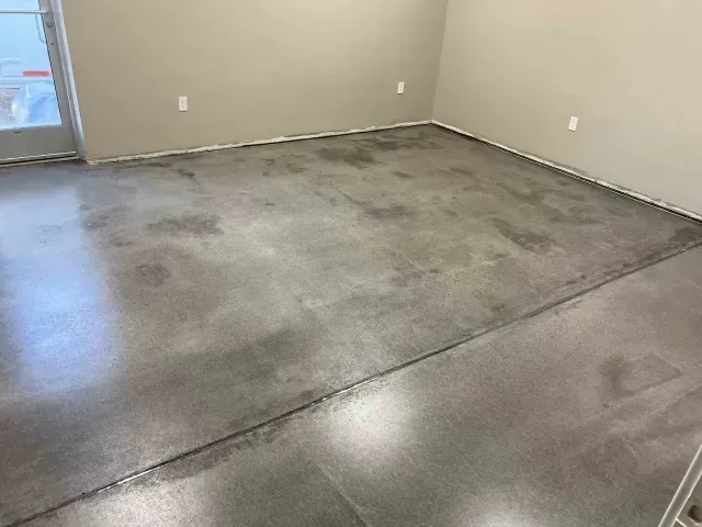 A room with a polished, grey concrete floor, beige walls, two electrical outlets, and a glass door on the left.
