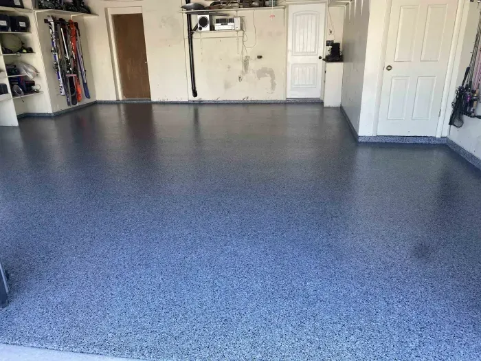 A garage with a clean, light blue speckled epoxy floor, white walls, and two closed doors.