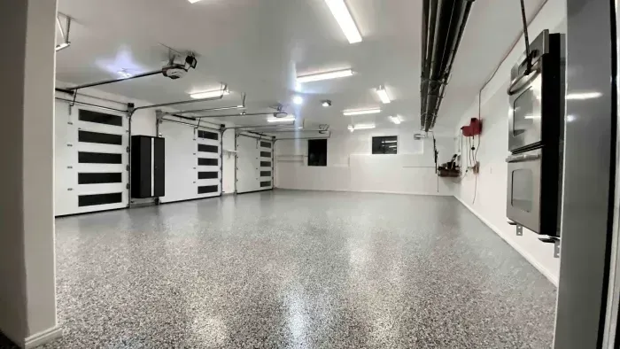 A spacious, well-lit garage with a speckled epoxy floor, multiple white garage doors, and a double oven mounted on the wall.