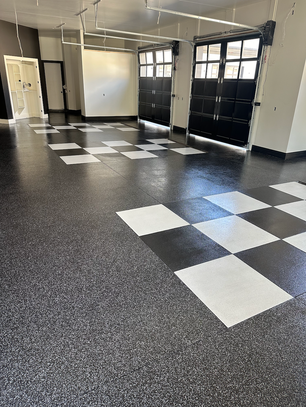 A person wearing spiked shoes uses a squeegee to spread light gray epoxy coating over a concrete floor.