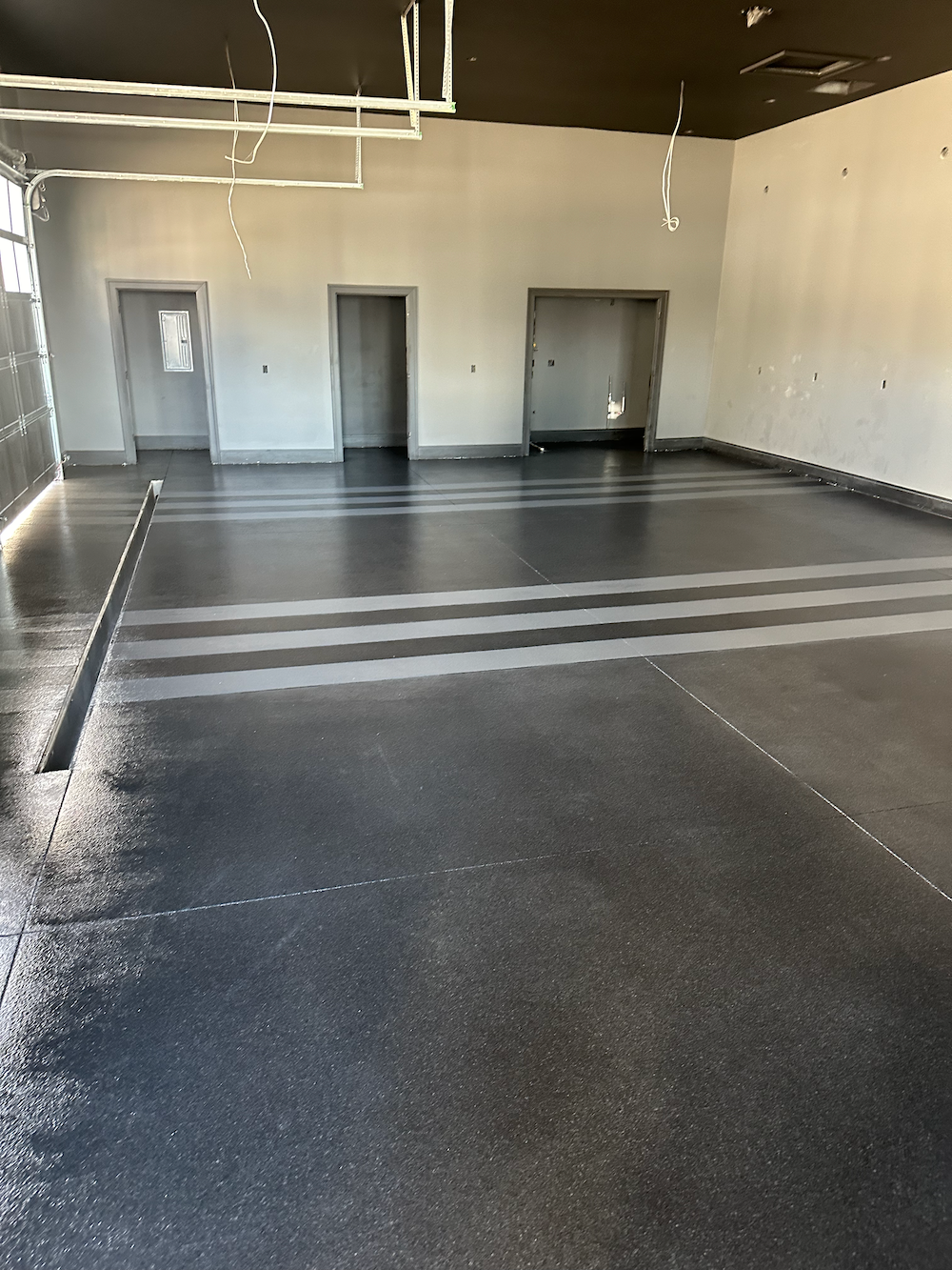 An indoor construction site with a speckled dark gray epoxy floor featuring light gray stripes leading to three doorways.