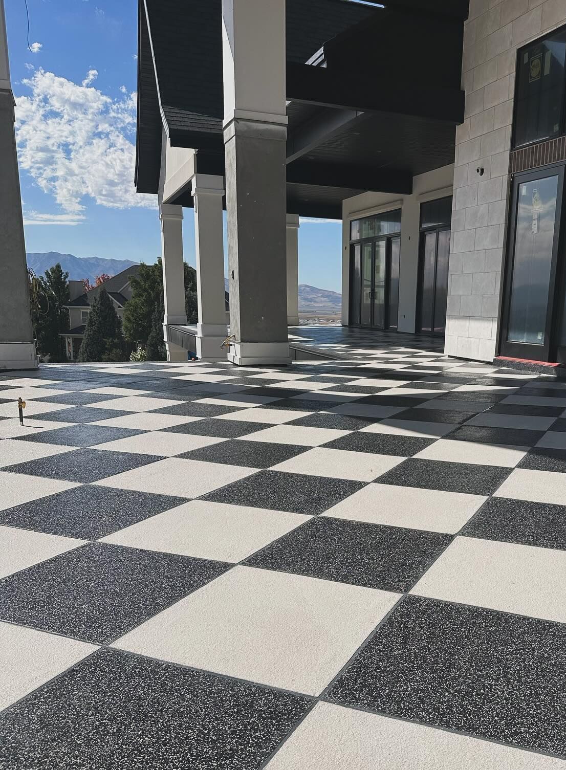 A patio with a black-and-white checkered floor under a covered porch overlooking mountains on a sunny day.
