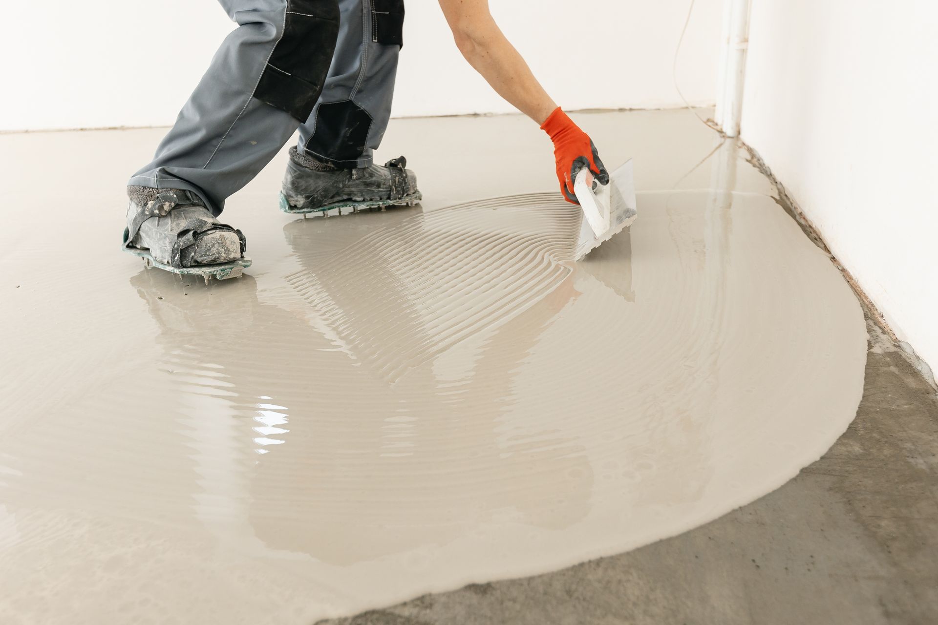 A person wearing spiked shoes levels wet concrete onto a floor with a trowel.