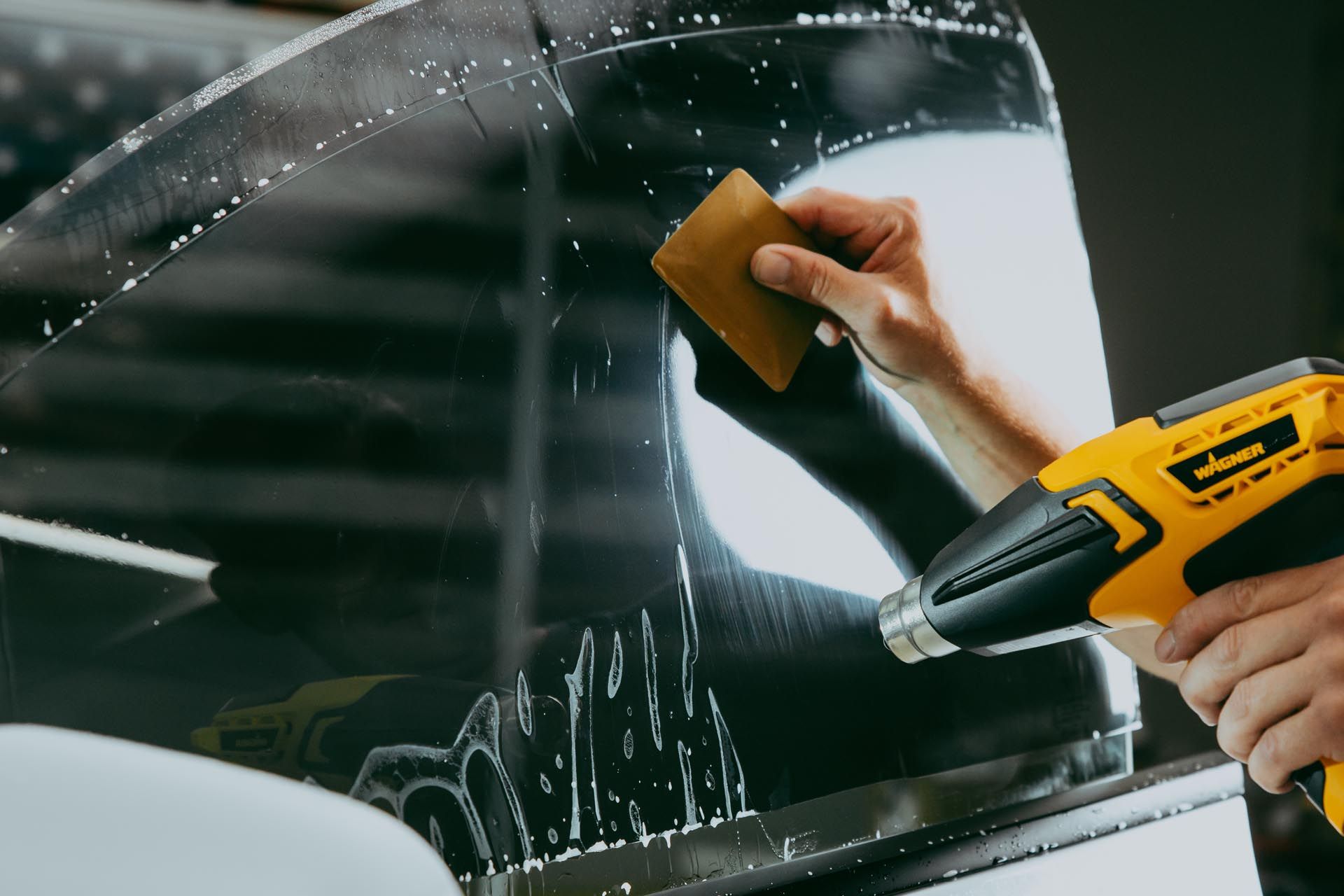 Person applying window tint to a car window with a heat gun and squeegee.