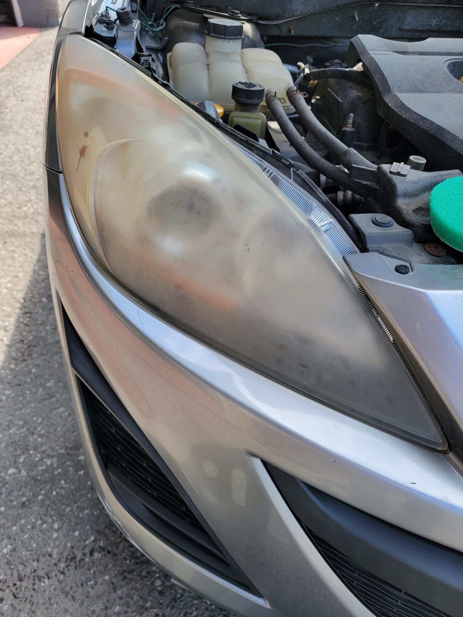 Cloudy car headlight on a silver vehicle; engine components visible in background.