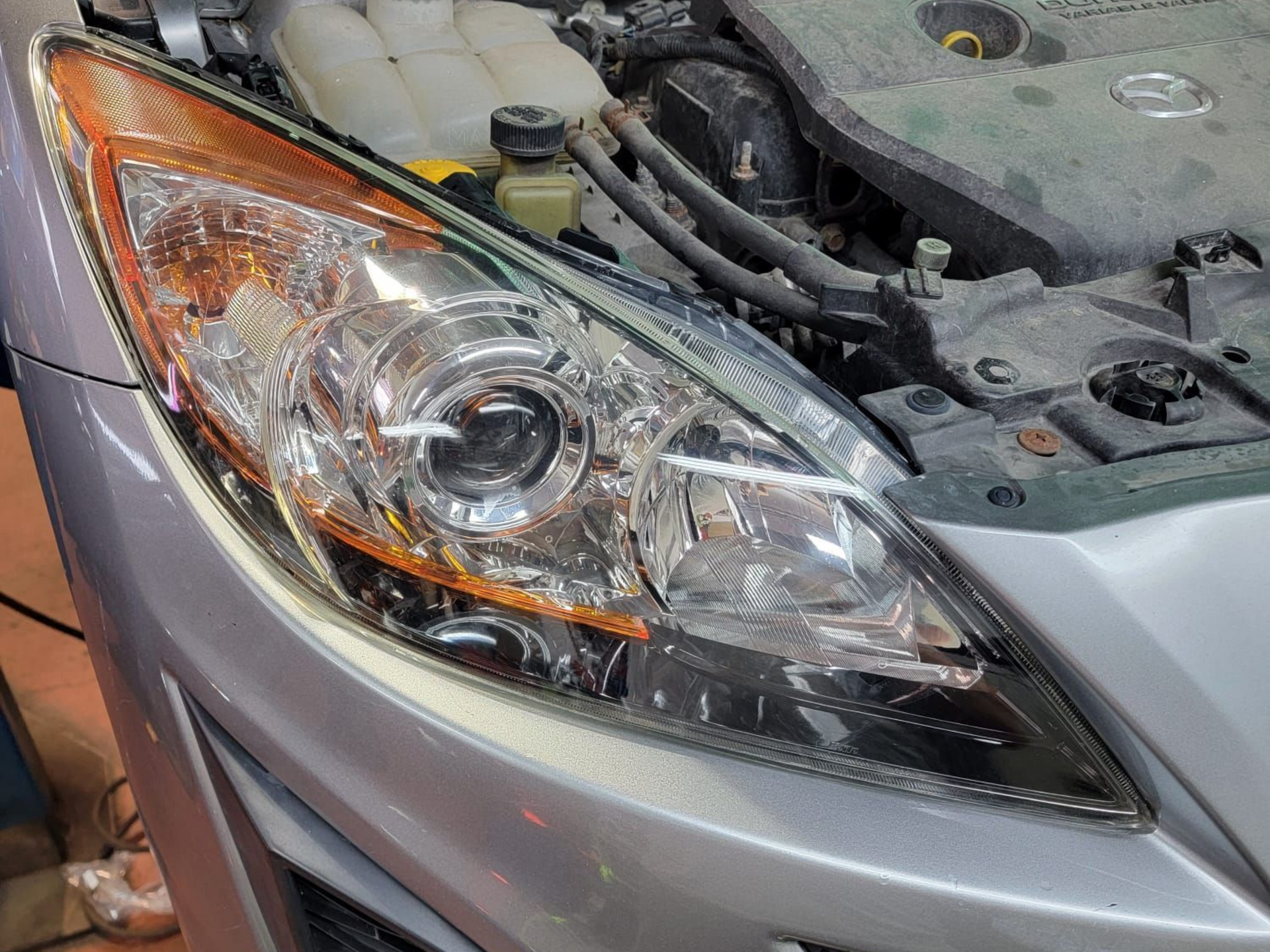 Silver car with open hood, showing headlight and engine.