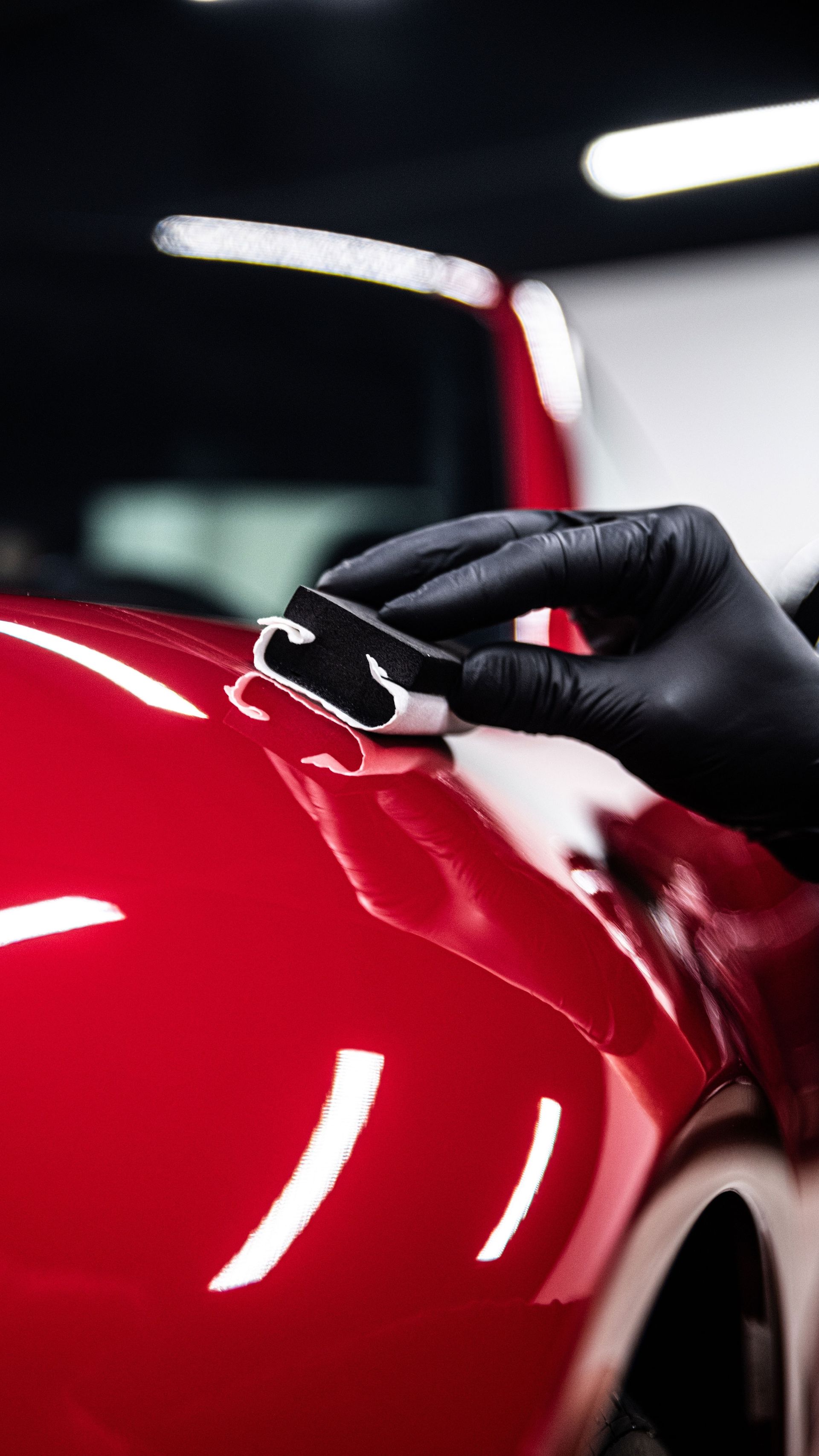 Gloved hand applying a coating to shiny red car paint.