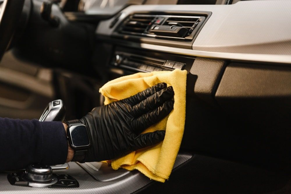 Gloved hand wiping a car dashboard with a yellow cloth.