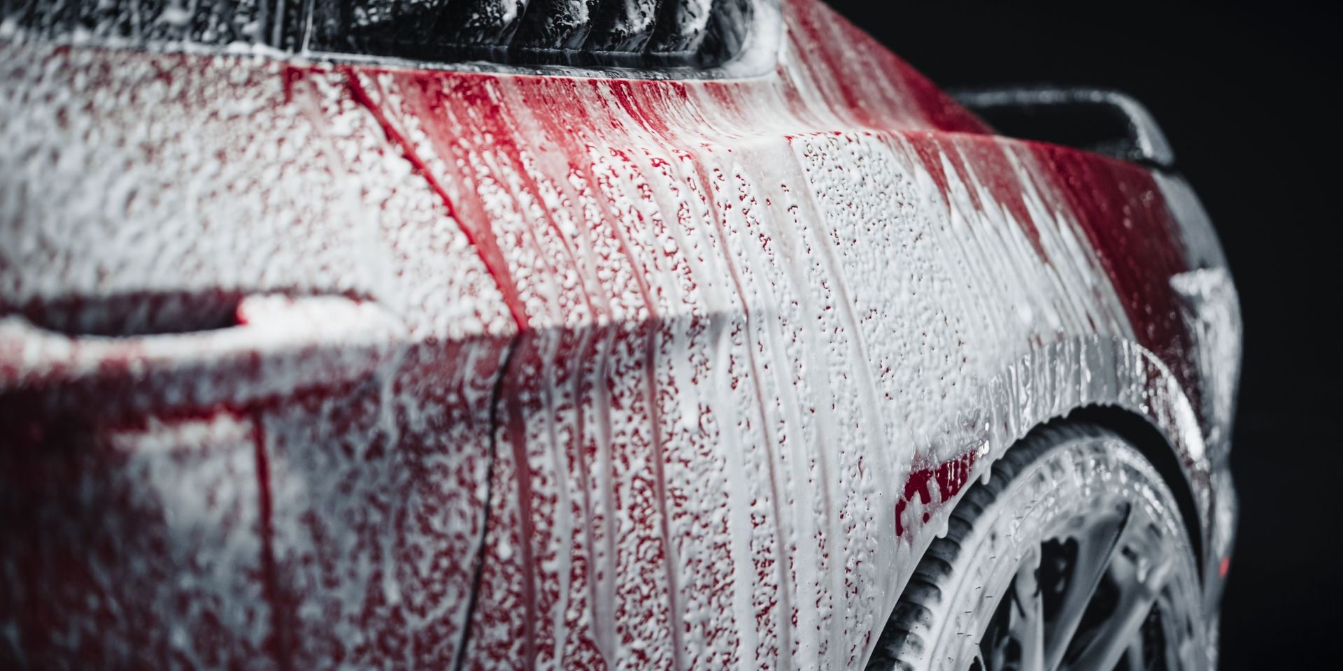 Red car covered in white foam, being washed.