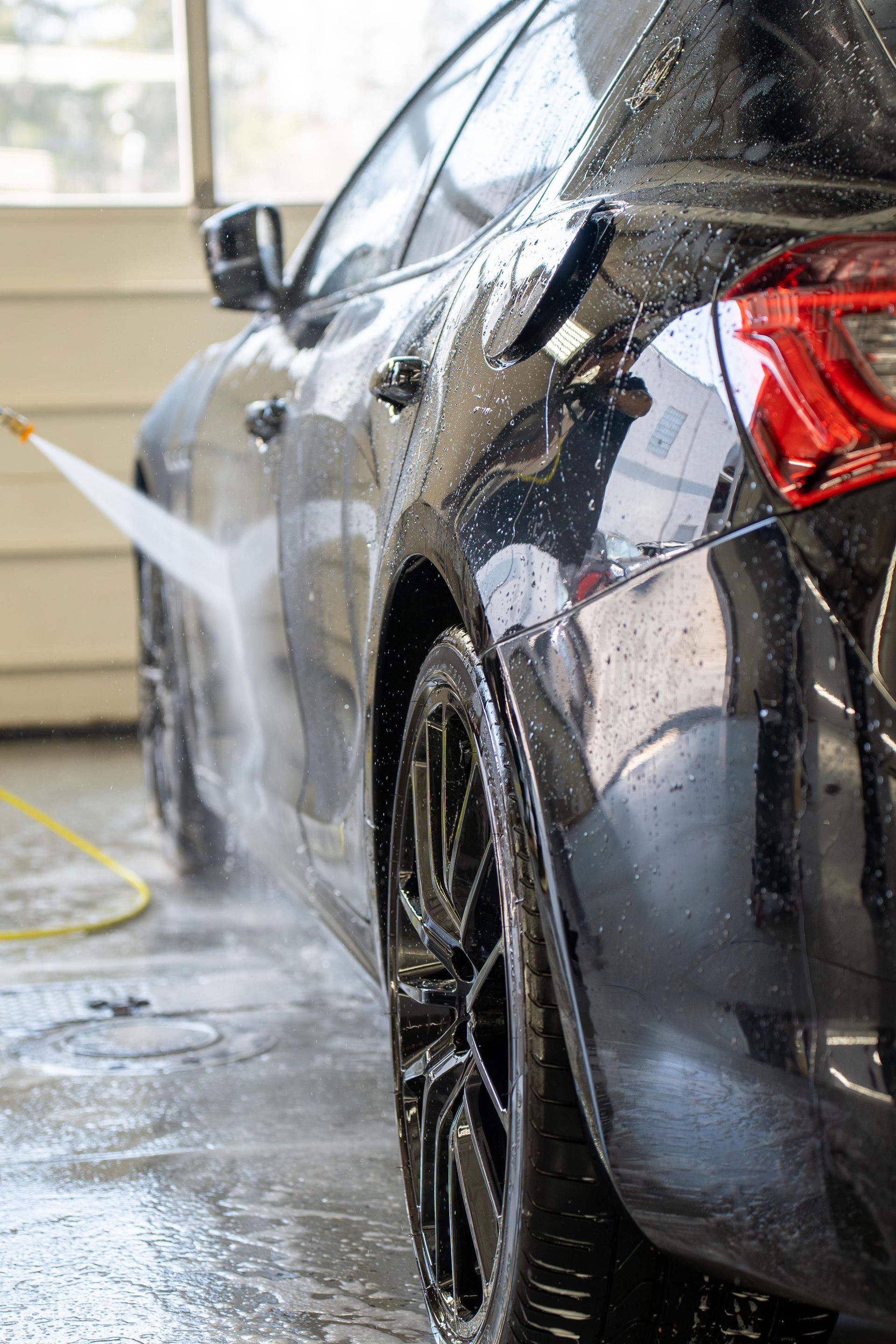 Black car being washed with a pressure washer, spraying water on the side panel and tire.