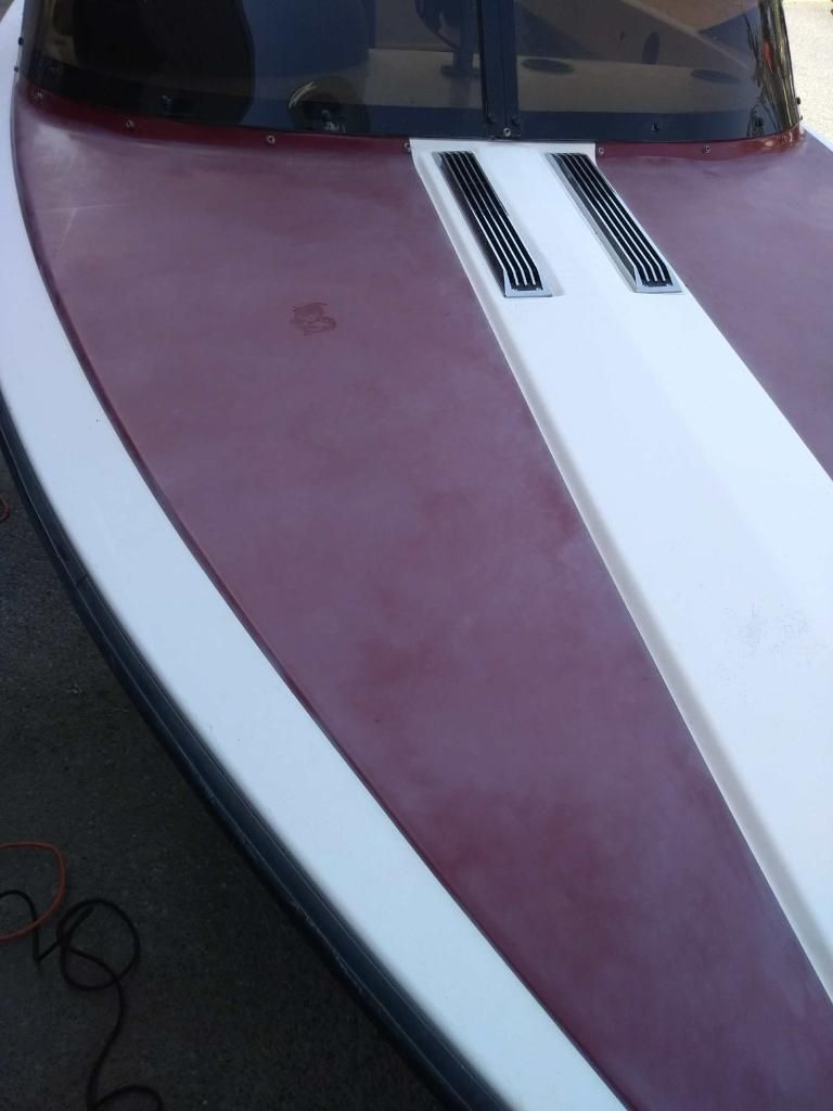 Boat bow, burgundy deck with white stripe, two black vents, dark windshield.