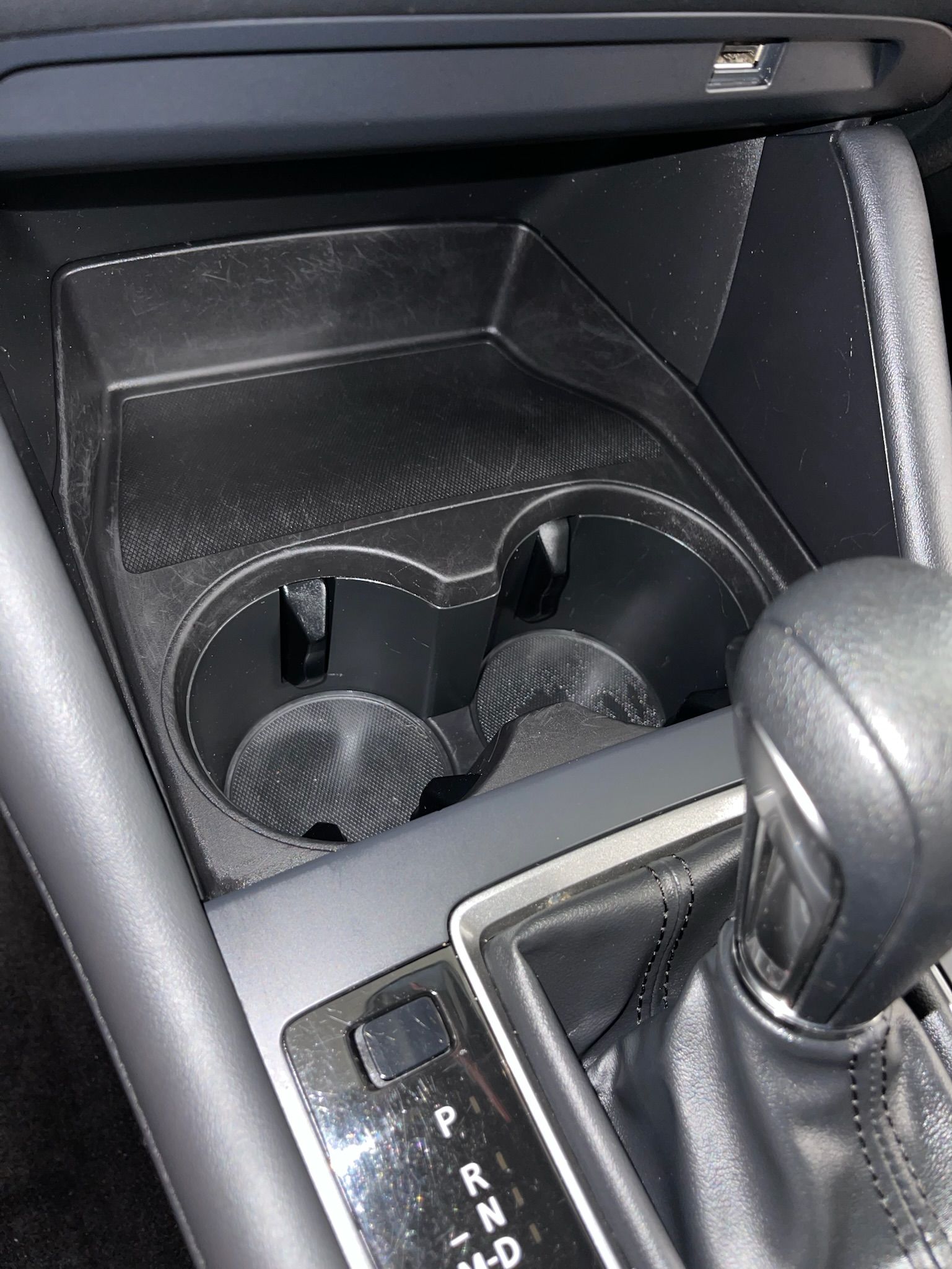 Car's center console with two cup holders, USB port, and gear shift. Black interior.