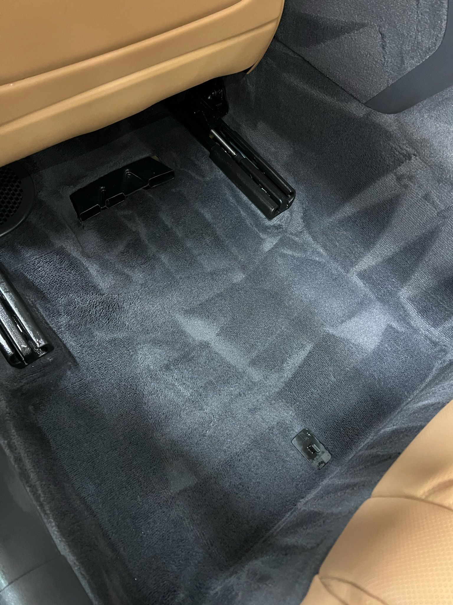 Gray car floor with tan seat trim and black seat rails.