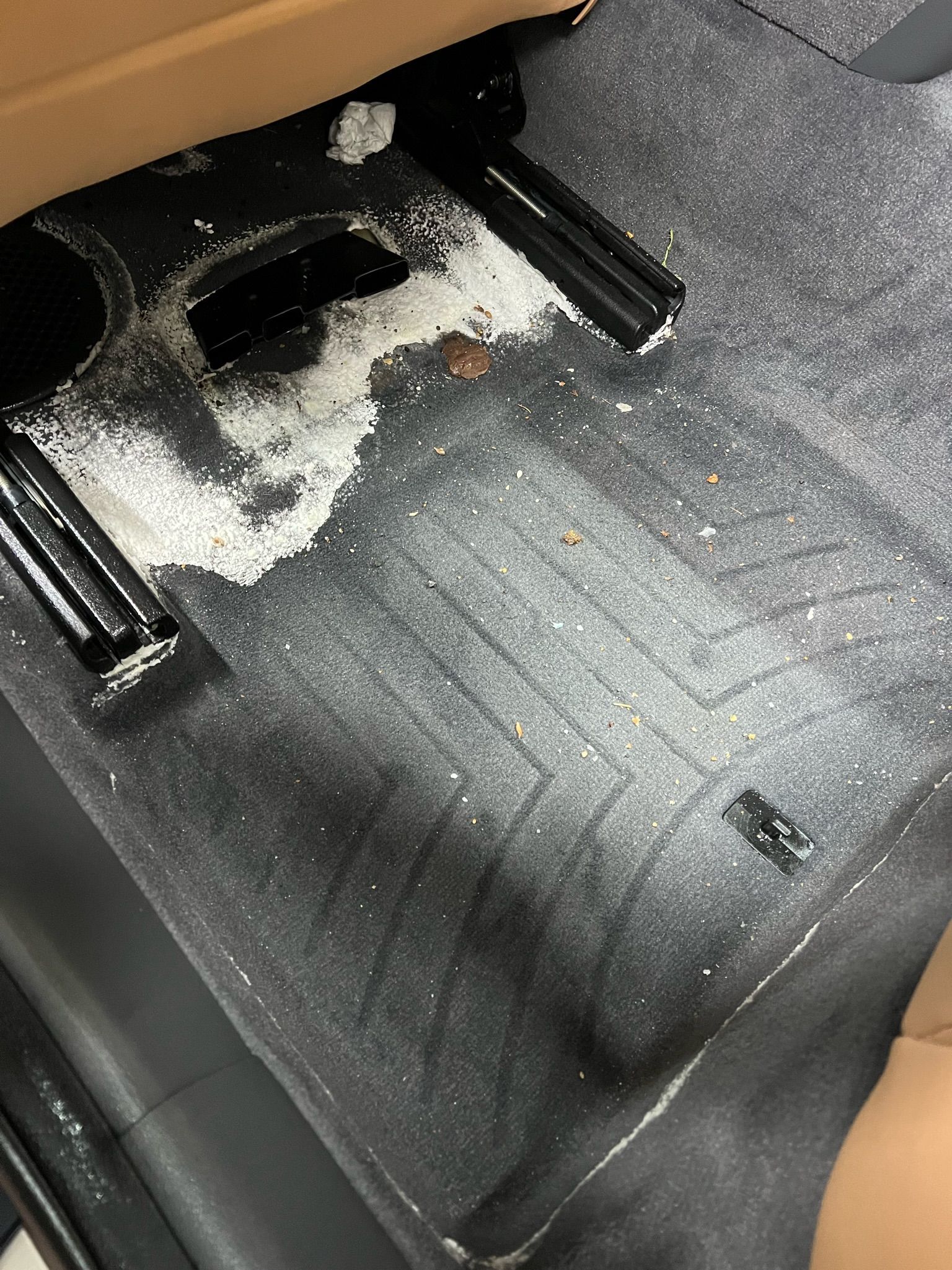 Gray car floor with white substance spilled near a seat track.