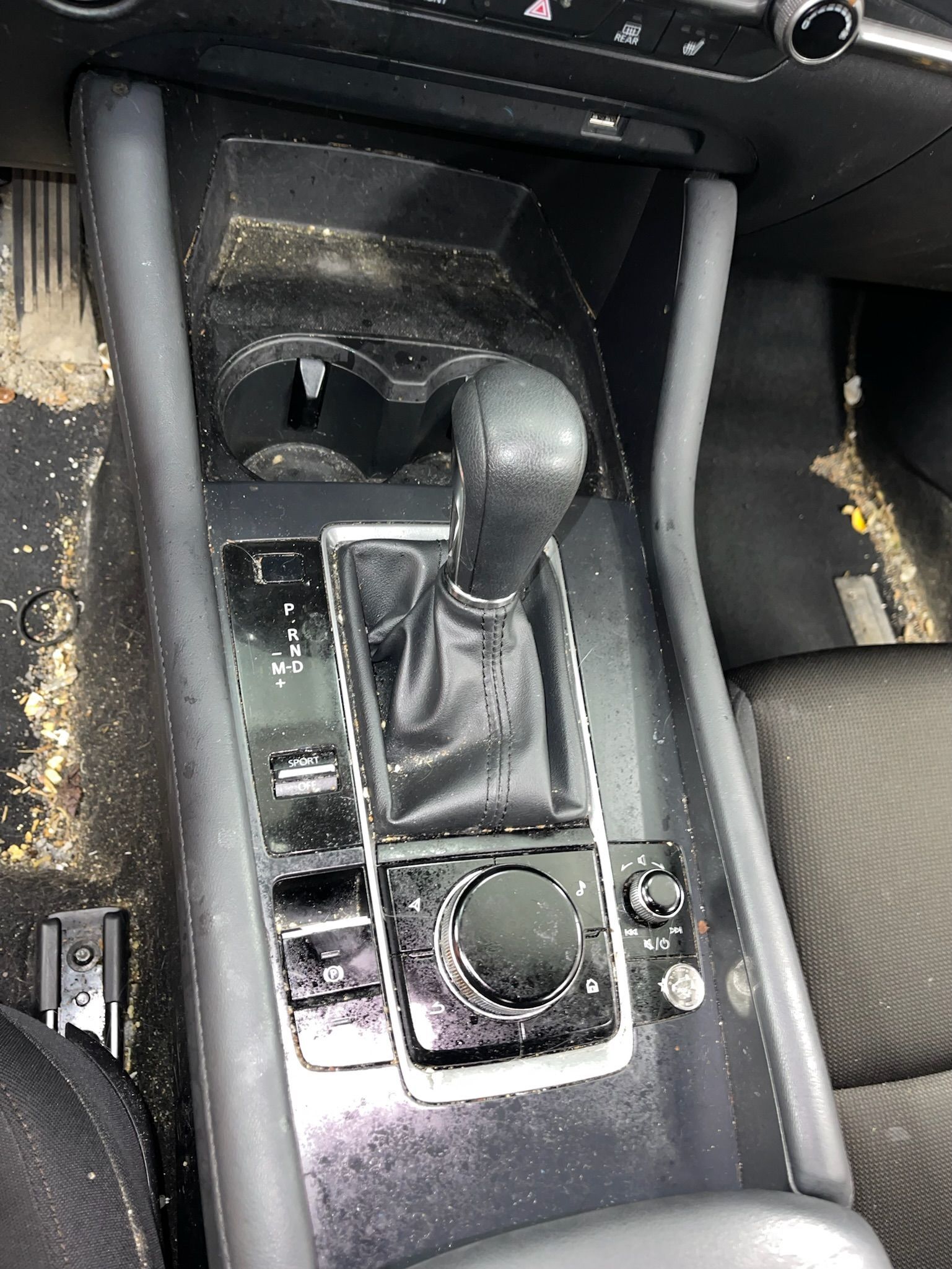 Dirty car console with gearshift, cupholder, and controls.
