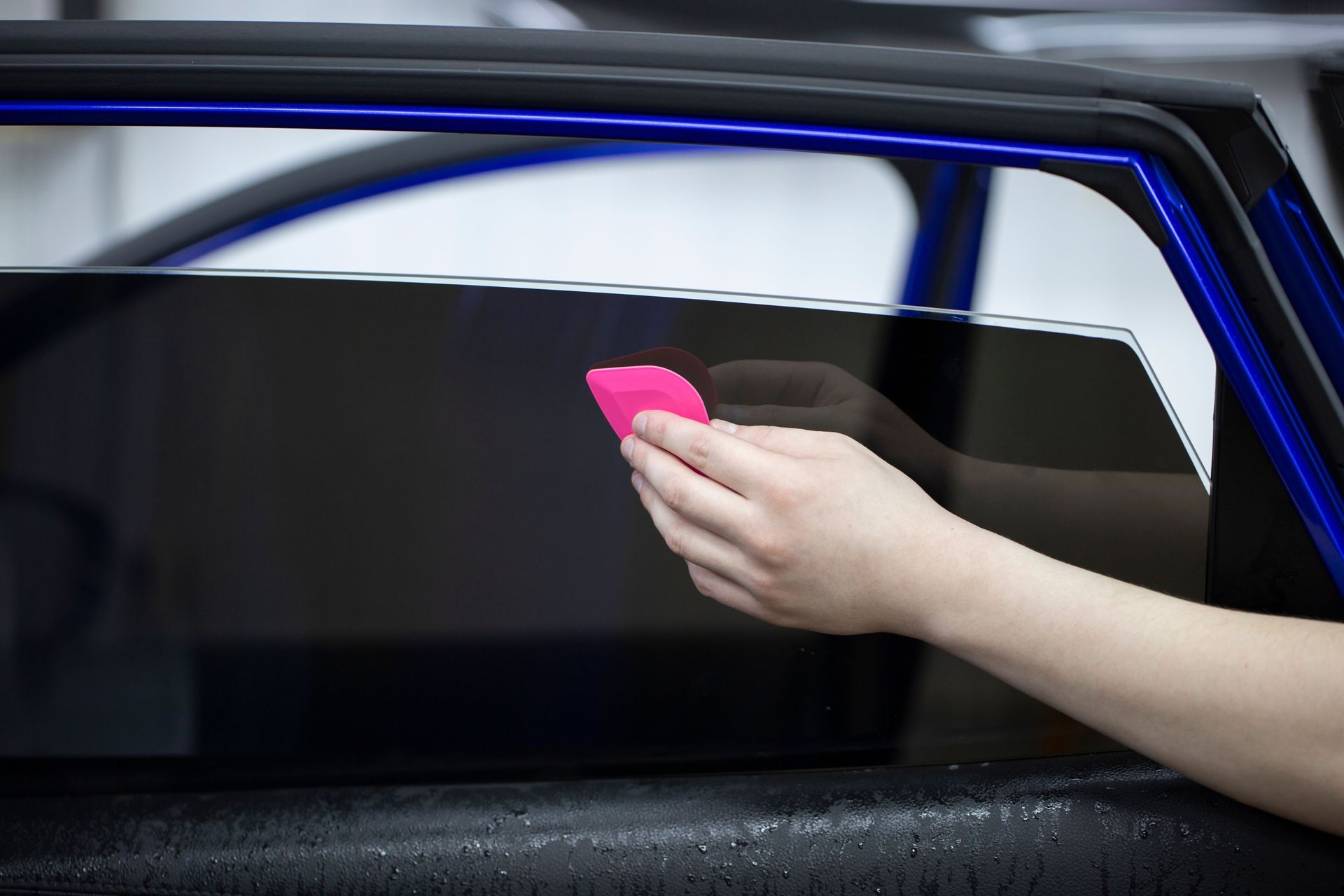 Hand applying tint to a car window with a pink tool.