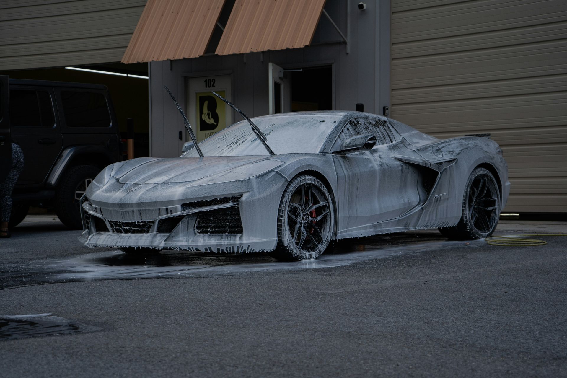 Grey sports car covered in white soap suds at a car wash.