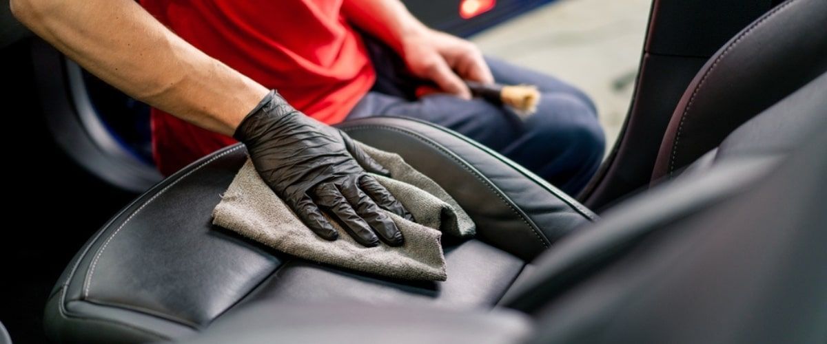 Person wearing black gloves cleaning a car seat with a cloth.