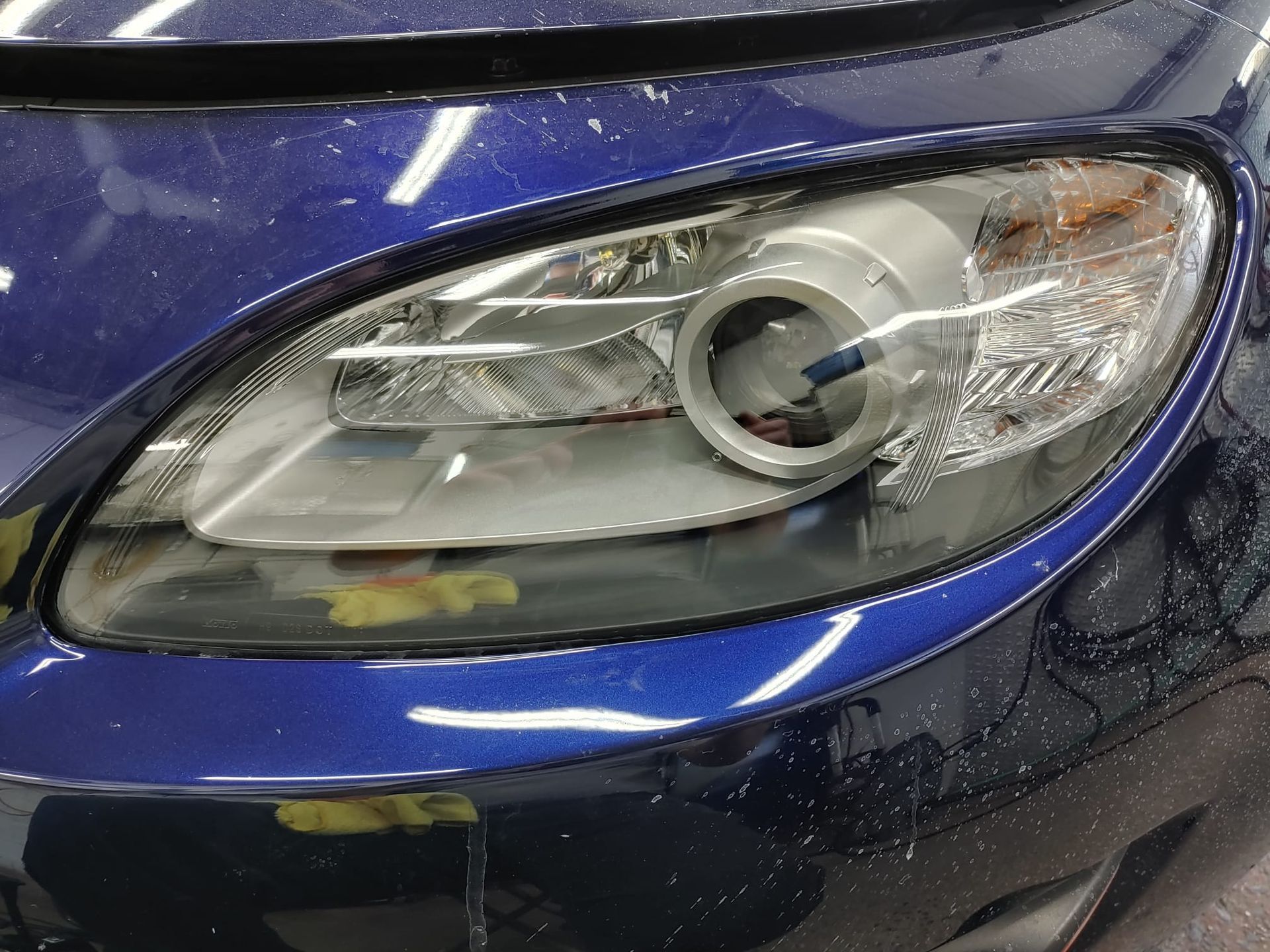 Close-up of a blue car's headlight. The headlight is oval-shaped and has a silver inner design.