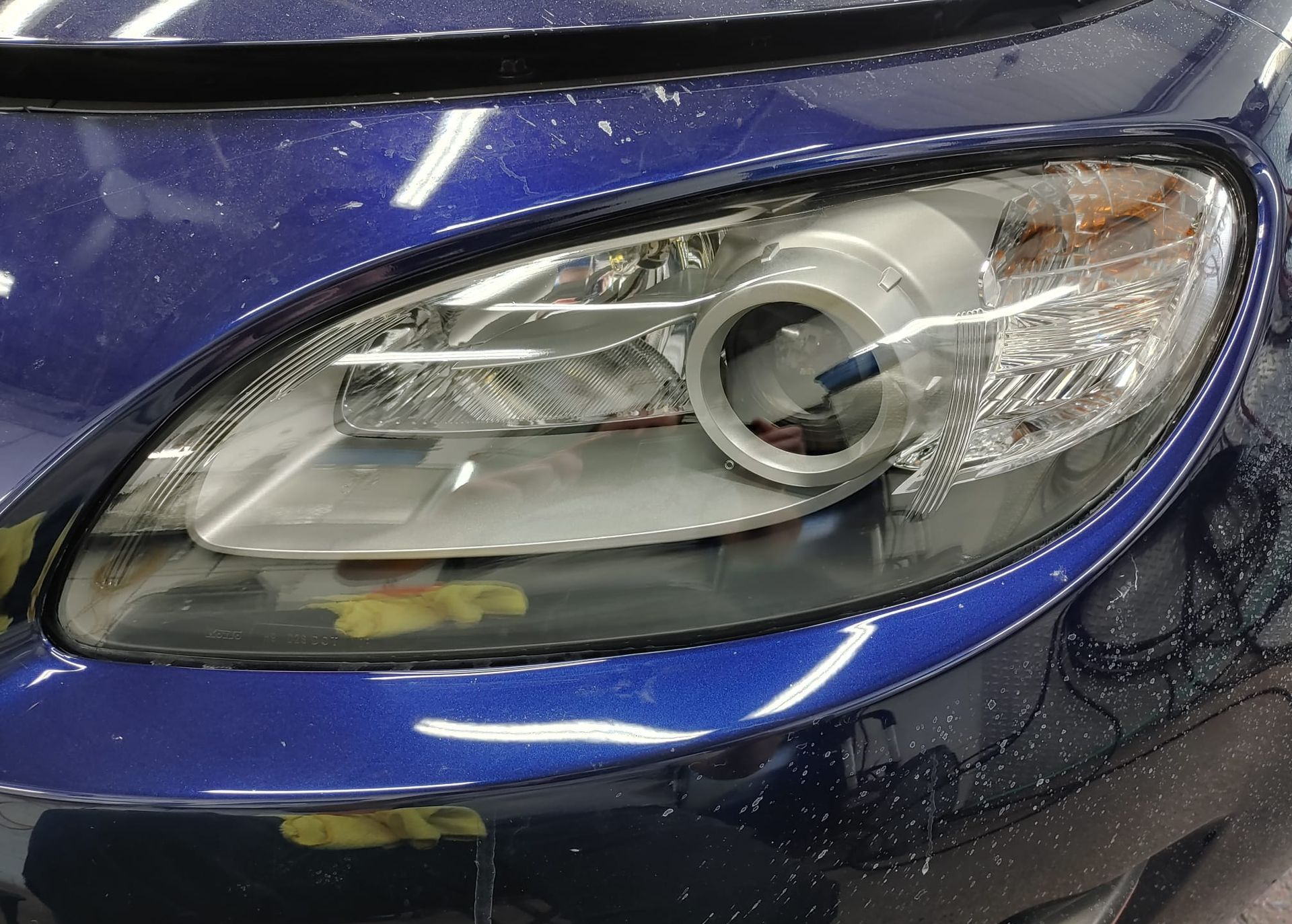 Blue car headlight, close-up. Shows the headlight lens and body panel.