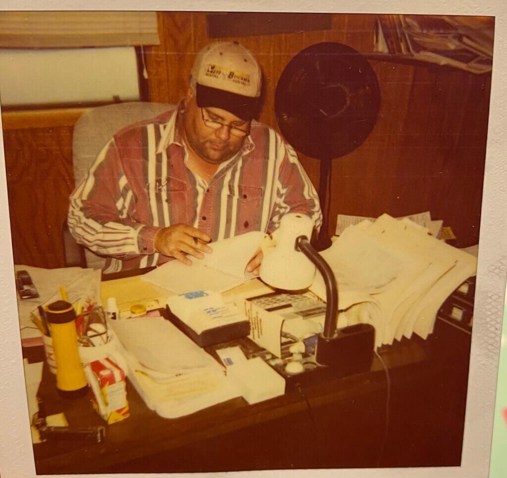 A man is sitting at a desk with a fan and papers
