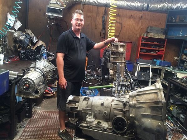 Person standing in a workshop beside a large engine transmission assembly