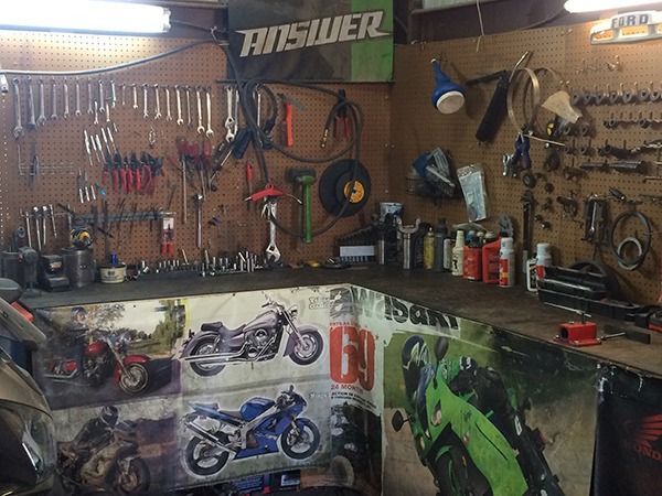 Motorcycle-themed garage workspace with tools, hanging gear, and racing posters on the walls