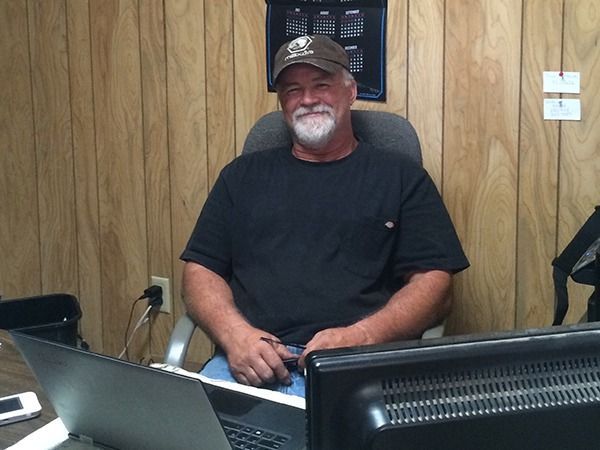 Smiling man in a black shirt seated at a desk in a wood-paneled office