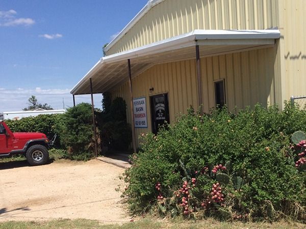 Yellow metal building with a porch, shrubs, and a red truck parked beside the entrance