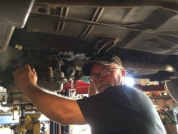 Mechanic working under a vehicle, inspecting parts with tools in a garage.