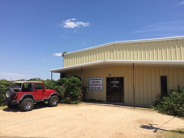 Red Jeep parked beside a beige metal building under a clear blue sky