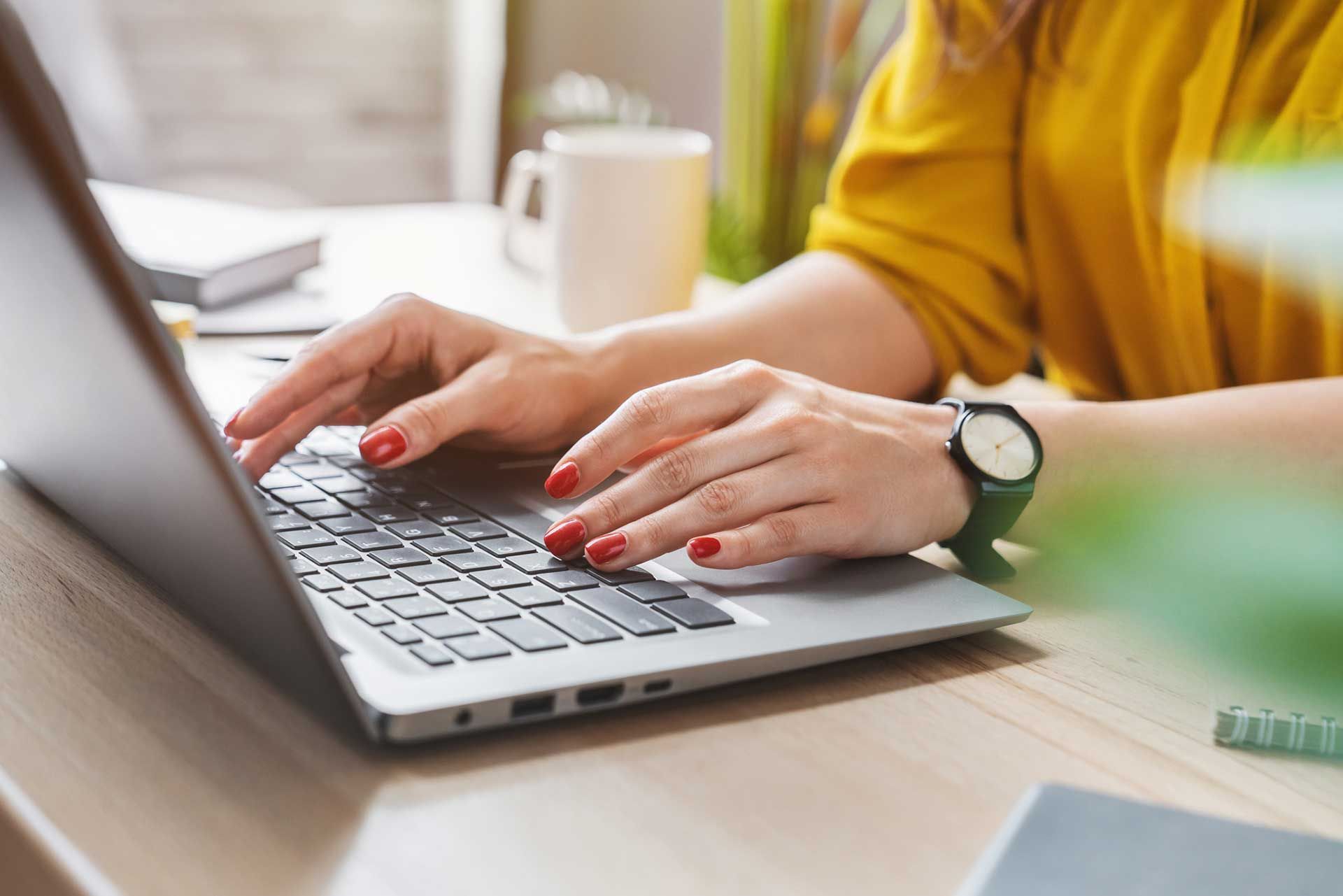 Woman typing on laptop with red nails and yellow top