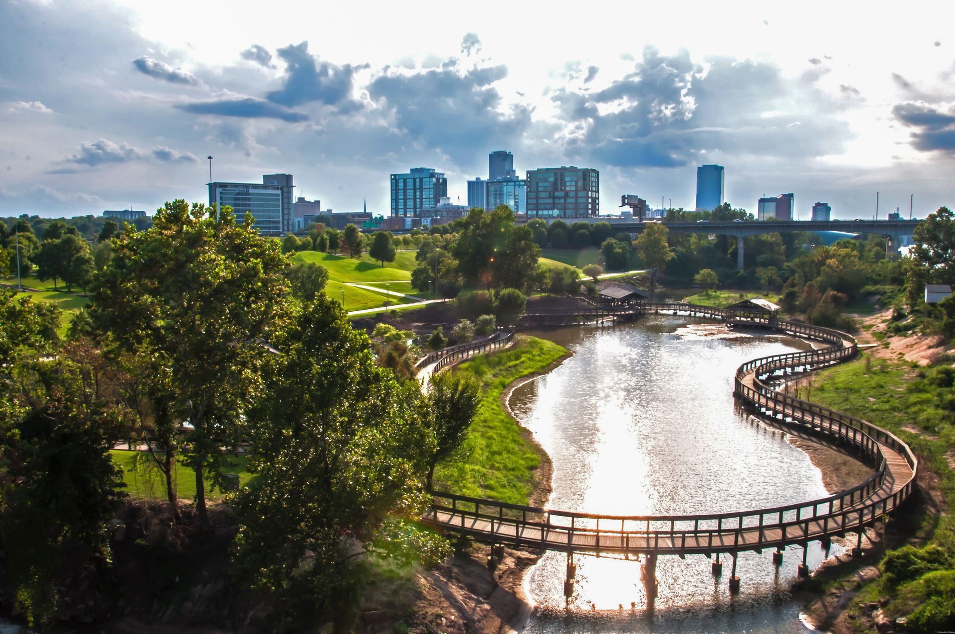 A bridge over a river in a park with a city in the background