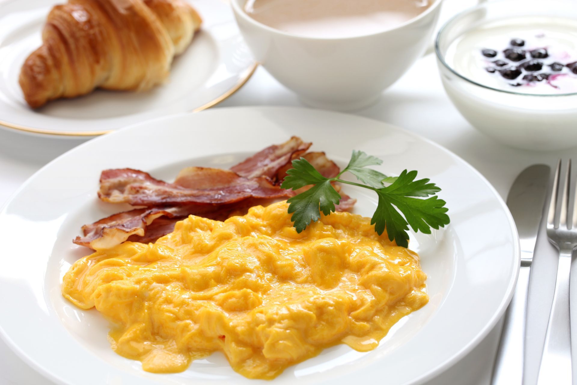 A plate of scrambled eggs with bacon and a croissant