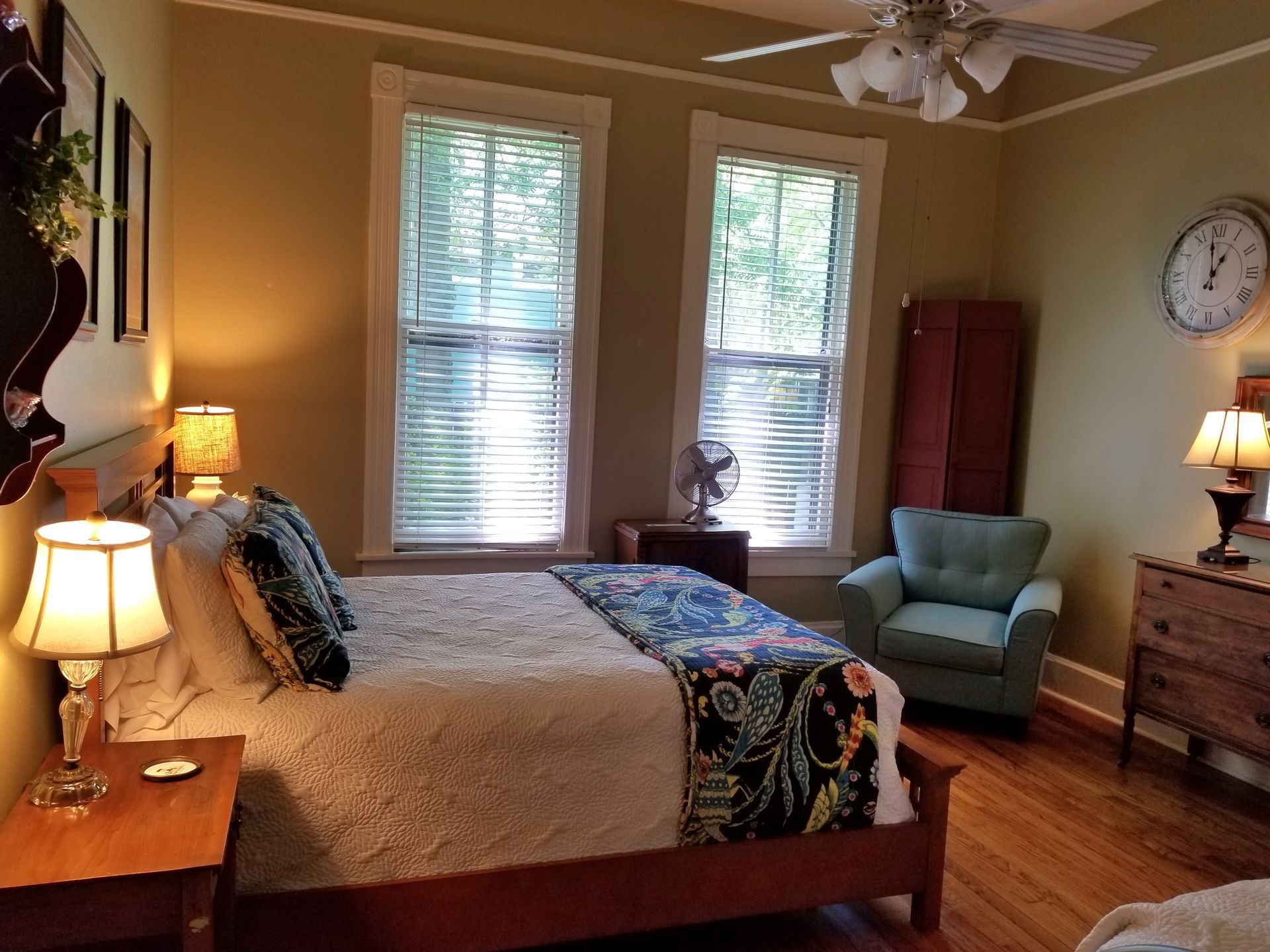 A bedroom with a bed , chair , dresser and a clock on the wall
