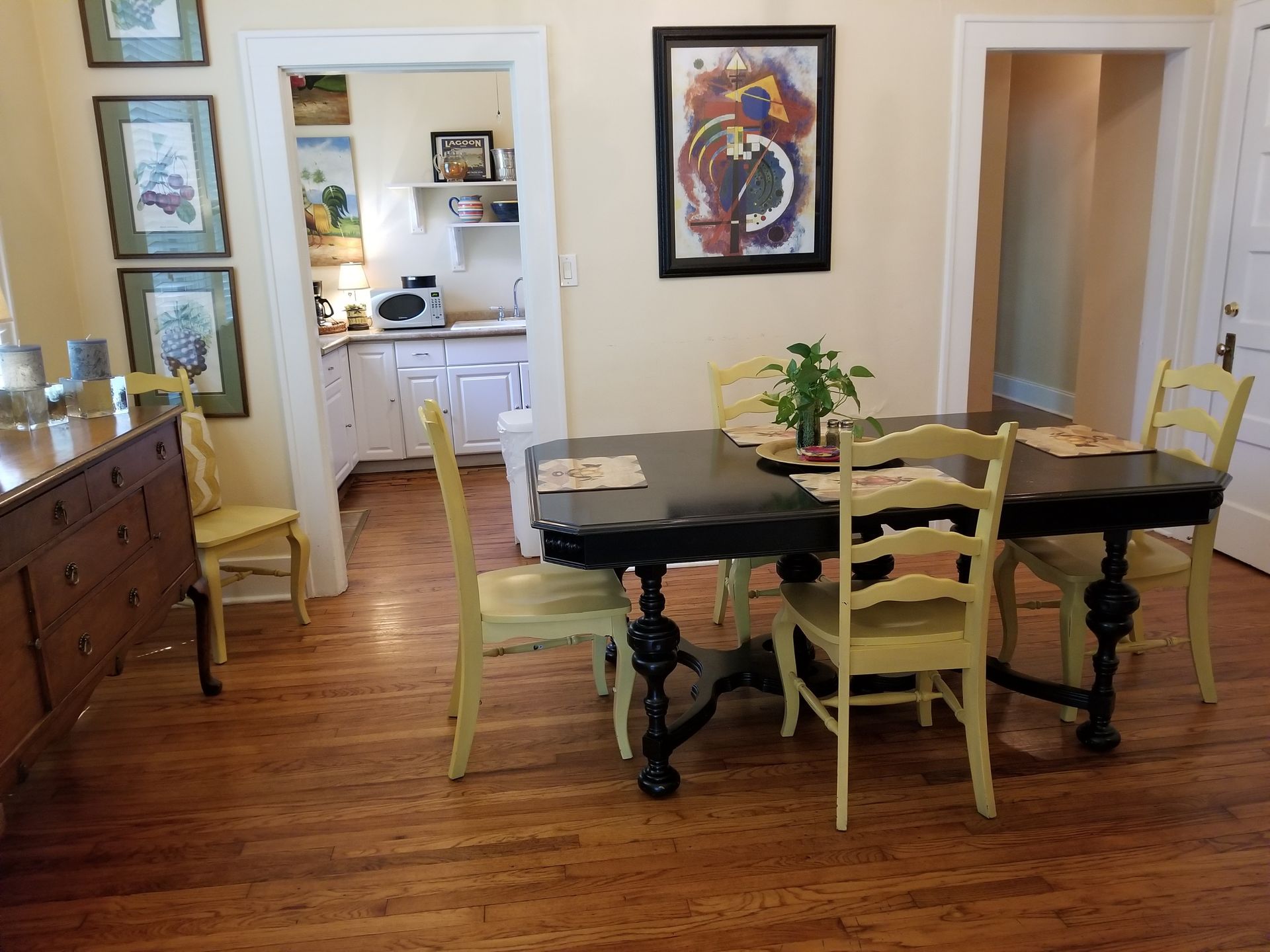 A dining room with a table and chairs and a painting on the wall.
