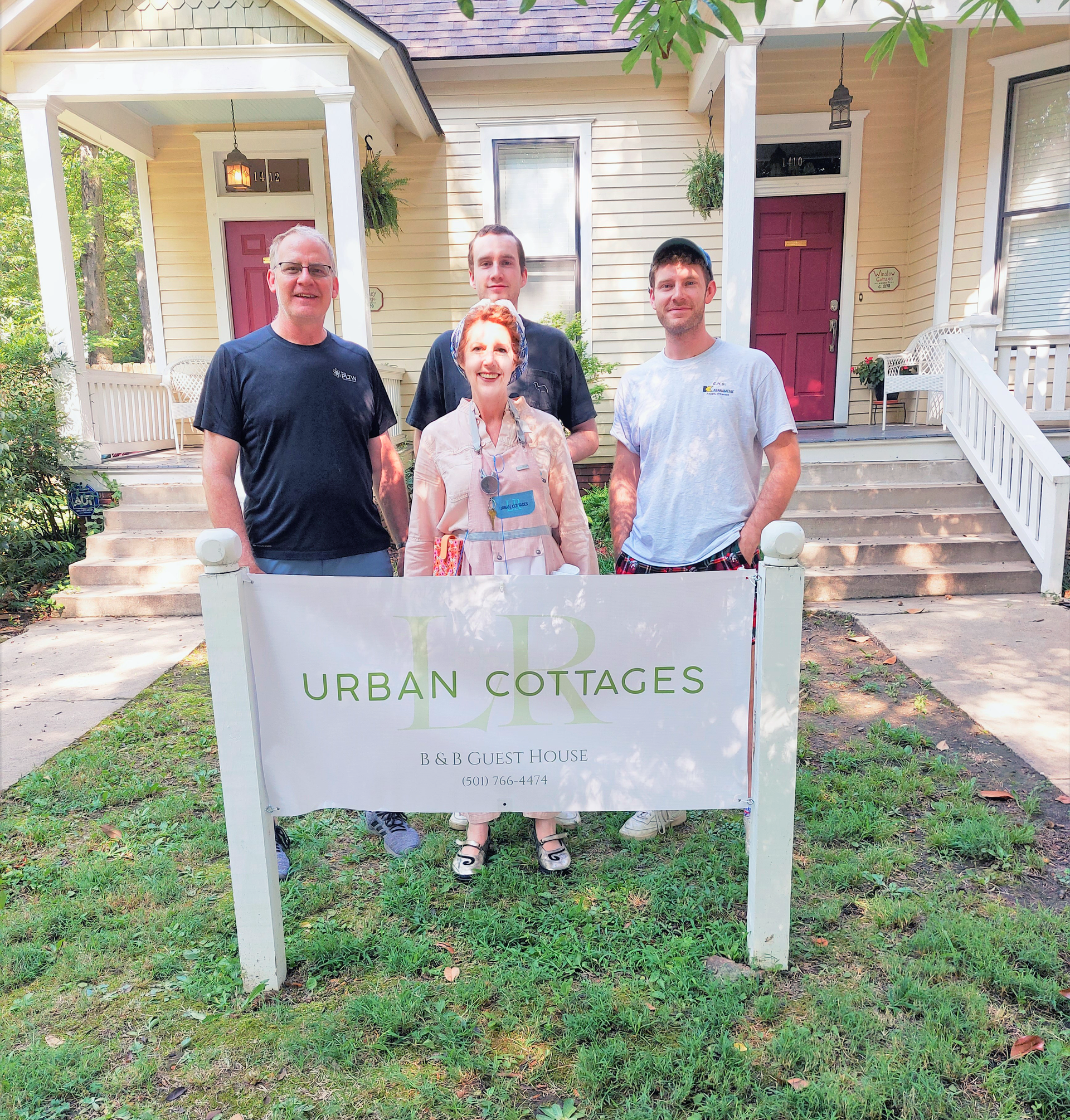 A group of people standing in front of a house holding a sign that says urban cottages